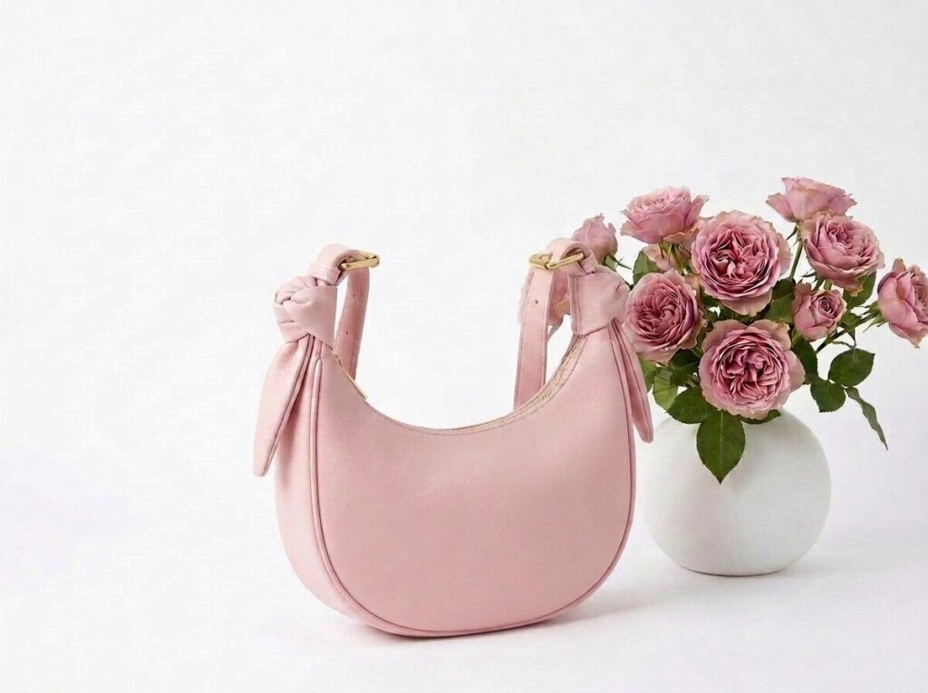 白い背景に置かれたピンクの三日月形のショルダーバッグと薔薇の花瓶。大きさ別の利点と難点